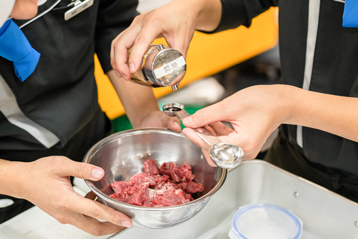 織田調理師専門学校_調理実習で肉に調味料を加えている様子